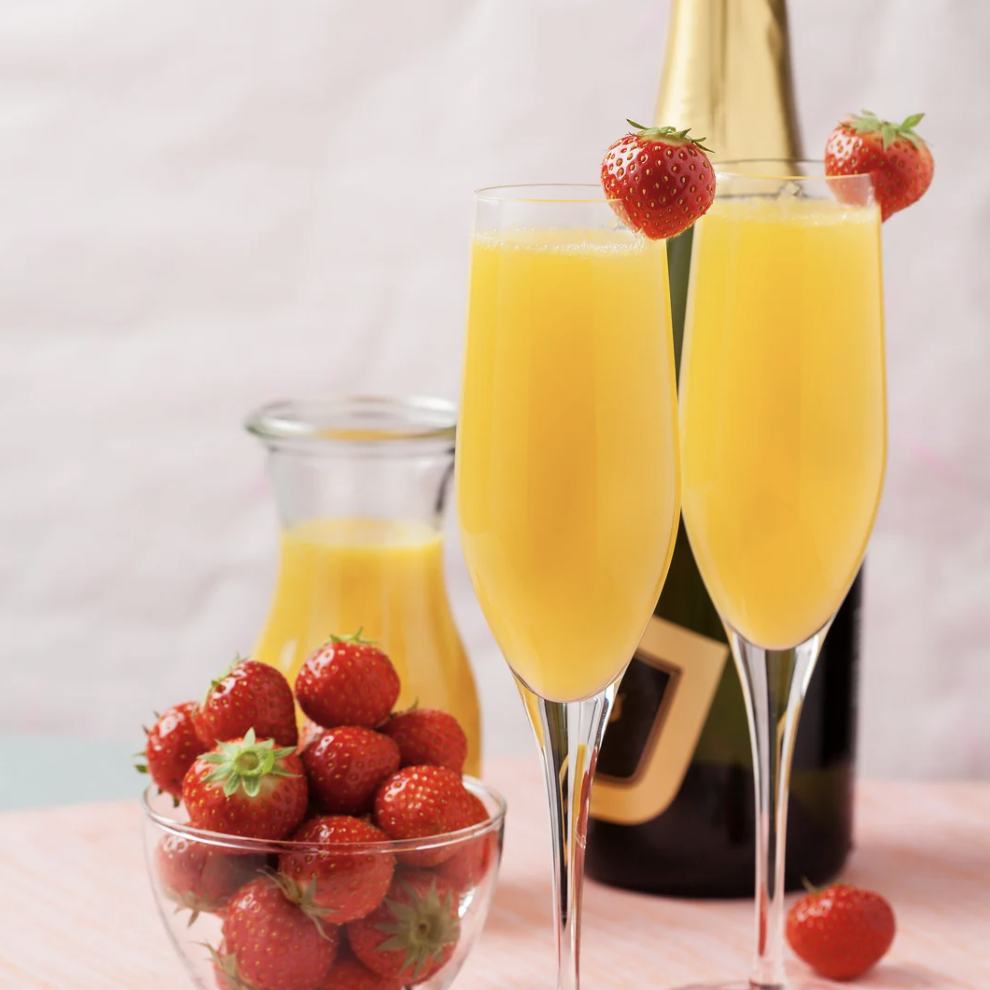 Two flutes filled with mimosas and garnished with strawberries